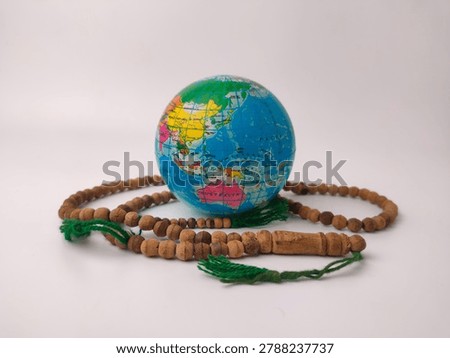 A small globe depicting a world map is surrounded by wrapped strands of brown wooden prayer beads with green tassels.