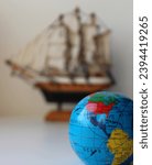 Small Globe With Mapped Travel Routes And Defocused Masted Ship Toy On Background
