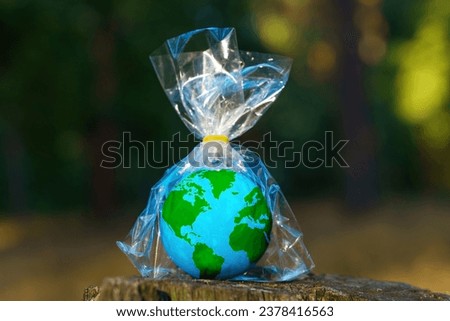 Small globe model encased in transparent plastic packaging perches on a forest stump. Plastic pollution and environmental consciousness related concept. Stock photo © 