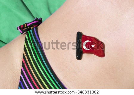 Small glossy ceramic Turkish flag lies on the stomach of a woman in a swimsuit