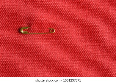 Small Golden Color Safety Pin Attached To Red Fabric Background. Copy Space