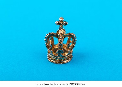 Small golden crown on blue paper background. Macro.
