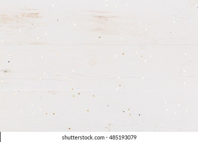 Small golden stars confetti on white wooden background.