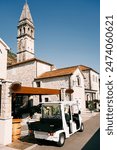 Small golf cart stands outside a restaurant near an old stone building overlooking the church bell tower