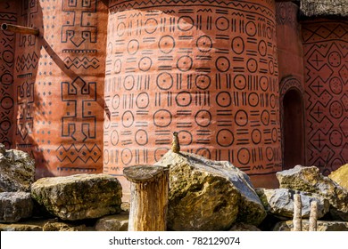 A small gopher standing on a stone, and in the background there is an painting African house
