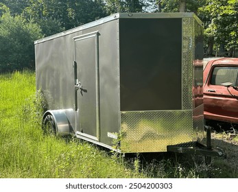 Small gray, enclosed trailer, parked in high grass next to an old brown SUV. - Powered by Shutterstock