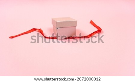 Small gray gift box is ajar and the red ribbon that tied the gift is untied.  Light pink pastel background. Copy space. Concept of preparing presents for the holiday.