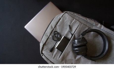 Small gray textile city backpack with laptop or ultrabook, power bank and wireless headphones. Traveling with gadgets. Close-up
