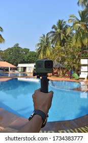 A small green colored action camera kept against a swimming pool to film it and for video logging with visible palm trees in the background