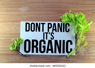 A small green plant with wooden background and a white paper with DONT PANIC ITS ORGANIC words