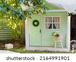 Small green shed garden house with window, door and chair outside. Kids playhouse, garden summerhouse background
