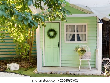 Small green shed garden house with window, door and chair outside. Kids playhouse, garden summerhouse background