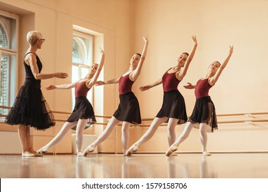 Small group of ballerinas practicing with their mature teacher at ballet studio. 
