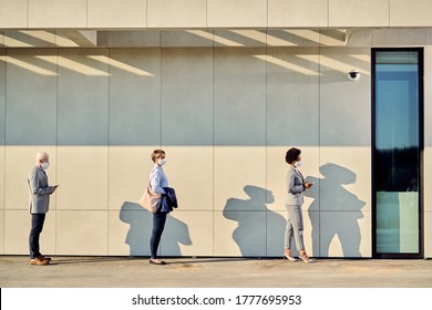 Small Group Of Business People With Protective Face Masks Standing Away From Each Other While Waiting Outdoors. Copy Space. 