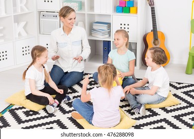 Small Group Of Children Sitting With Crossed Legs And Clapping Hands In A Circle During Classes With Their Teacher