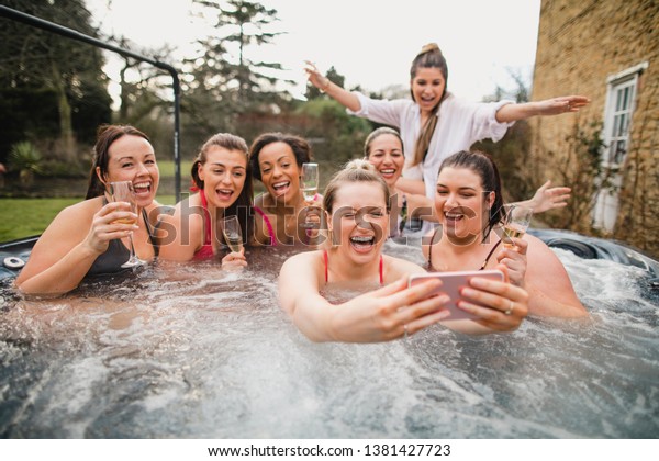 Small group of\
female friends enjoying a weekend away. They are taking a group\
selfie while sitting in a hot\
tub.