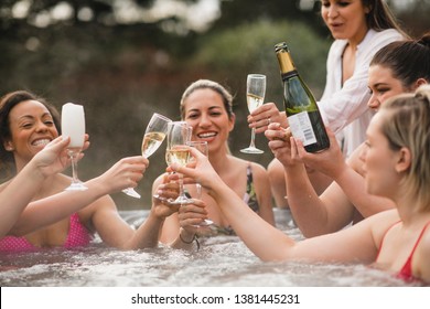 Small group of female friends socialising and relaxing in the hot tub on a weekend away. They are celebrating with a glass of champagne. - Shutterstock ID 1381445231