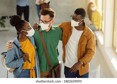 Small Group Of Happy College Friends With Protective Face Masks Embracing While Standing In A Lobby And Talking. 