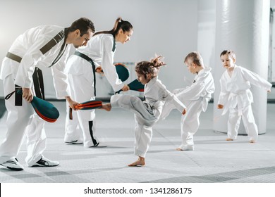 Small group of kids in doboks practicing with their trainers taekwondo moves while kicking in kick target.