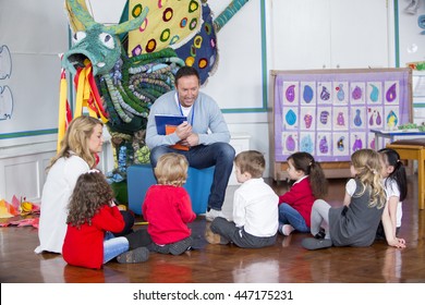 Small group of nursery children are sitting on the floor in the school hall around their teacher. He is holding books and talking to them.  - Powered by Shutterstock