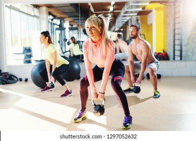 Small Group Of People With Healthy Habits Swinging Kettlebell. Gym Interior, Mirror In Background.