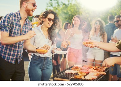 Small group of people standing around barbecue grill at outdoor party - Shutterstock ID 692905885