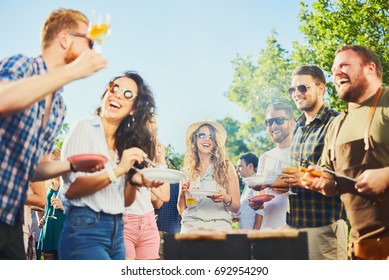 Small Group Of People Standing Around Barbecue Grill At Outdoor Party 