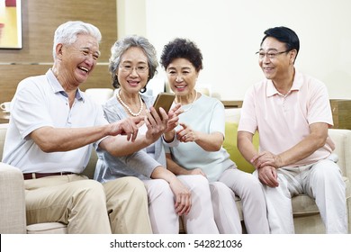 Small Group Of Senior Asian People Sharing Content In Cellphone During Gathering.