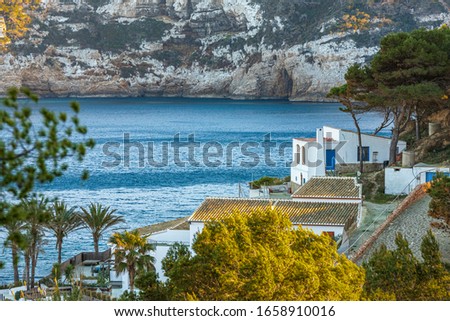 Small group of traditional Mediterranean withe houses near the beach and the Mediterranean sea surrounded by a cliff and a Mediterranean forest