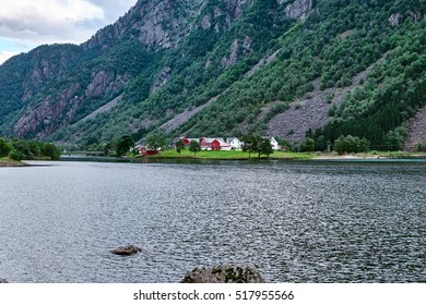 Small group of wood houses on a small piece of flat land in the lake Sandvevatnet between mountain sides in Hardanger in Norway - Powered by Shutterstock