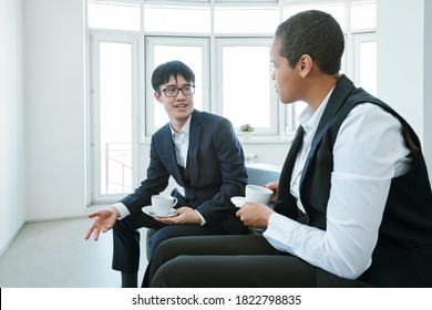 Small Group Of Young Elegant Contemporary Intercultural Business Partners In Formalwear Discussing Details Of Reports After Conference