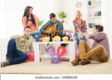 Small Group Of Young People At The Home Party, Enjoy The Sounds Of The Acoustic Guitar, Drinking Wine And Beer.