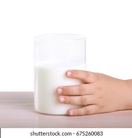 A Small Hand Of A Little Child Is Holding A Large Glass Of Organic Milk, Which Stands On A Wooden Table Isolated On A White Background.