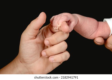 The small hand of a newborn caucasian baby grasps the hand of an adult person.