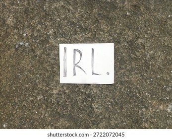 A small, handwritten note, resting on a rough concrete surface, emphasizing a non-digital concept, featuring the specific abbreviation 
