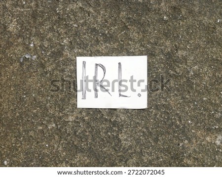 A small, handwritten note, resting on a rough concrete surface, emphasizing a non-digital concept, featuring the specific abbreviation 