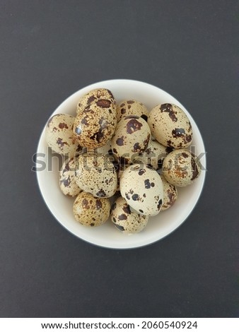 Small hard boiled quail eggs in the white ceramic bowl. Black background. Locally known as telur puyuh. Speckled brown on the surface. Avian small size eggs. Malaysia.