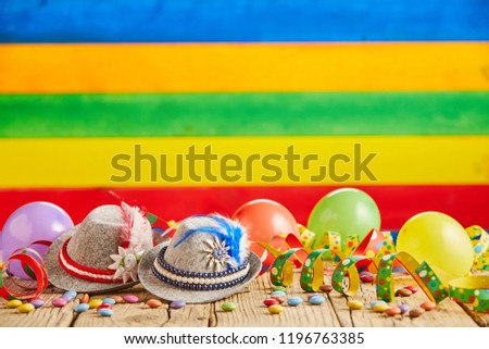 Small hats with feathers and spotted celebration ribbons next to round balloons in front of striped background