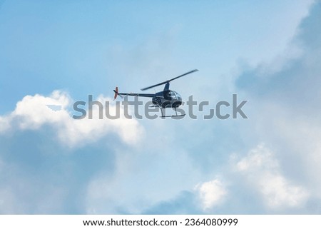 A small helicopter flies through the cloudy sky