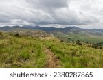 A small hiking trail high up in the Drakensberg Mountains of South Africa, with storm clouds gathering over the distant blue peaks in the background