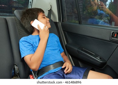 Small Hispanic Boy Talk On Phone In Back Seat Of Car