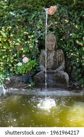 Small Home Garden Fountain With Buddha Statue Between Trees And Bushes