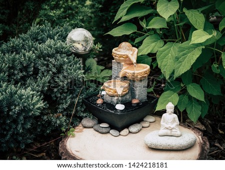 Small home garden private fountain with buddha statue between trees and bushes. Private zen garden concept, modern dark green color retouch.