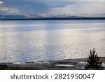 Small hot spring pool on the shoreline of Yellowstone Lake at dusk, a low crater rim of gray mineral crust holding still water at the water