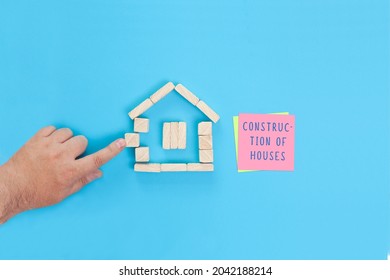 A Small House Made Of Wooden Blocks And A Sticky Note With The Words Construction Of Houses. Concept For A Construction Company Or Real Estate Construction.