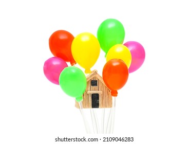 Small house model in a cluster of multicolored balloons isolated on a white background. Creative real estate related concept.