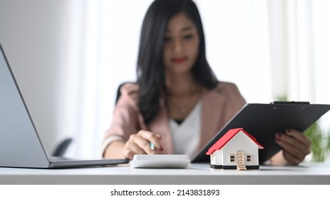 Small House Model On White Table And Professional Financial Advisor Is Using Calculator.