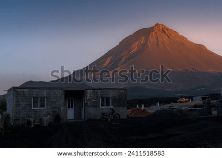 The small house with motorbike on the lava field in front of Pico do Fogo volcano during the scenic sunset at Fogo island, Cape Verde.