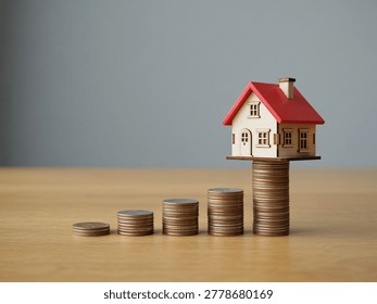 A small house sits atop a stack of coins representing financial growth