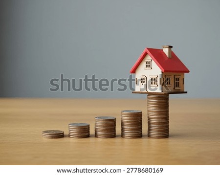 A small house sits atop a stack of coins representing financial growth